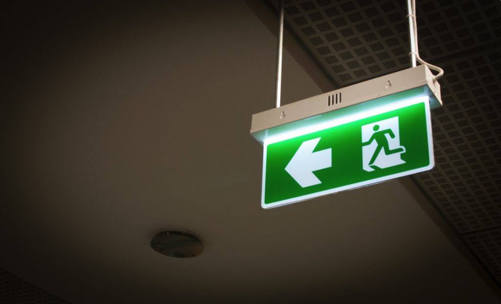 Illuminated green emergency exit sign suspended from a commercial building ceiling