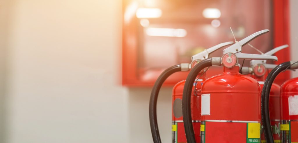 Red fire extinguishers ready for inspection beside a wall-mounted fire alarm panel