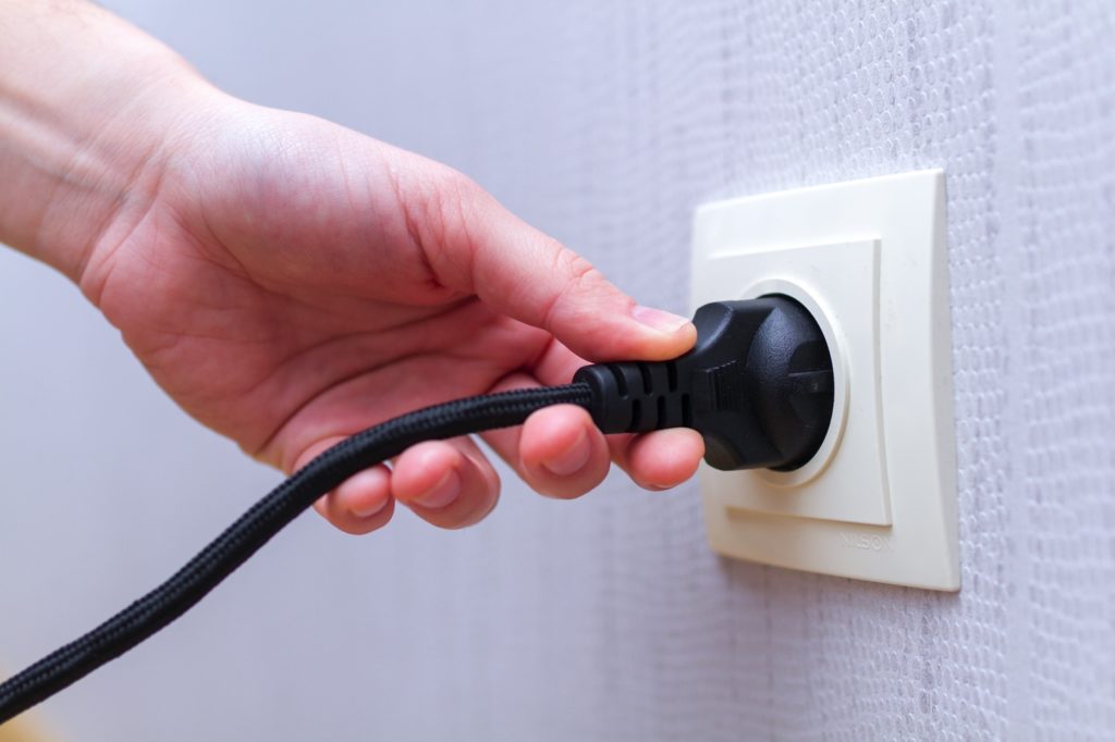 Hand plugging an electrical cord into a wall outlet for electrical safety inspection
